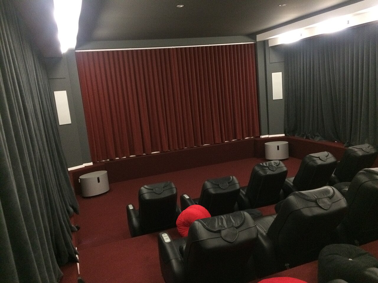 A dedicated cinema room with acoustic panelling, heavy curtains and two tiered rows of recliner seating facing a screen