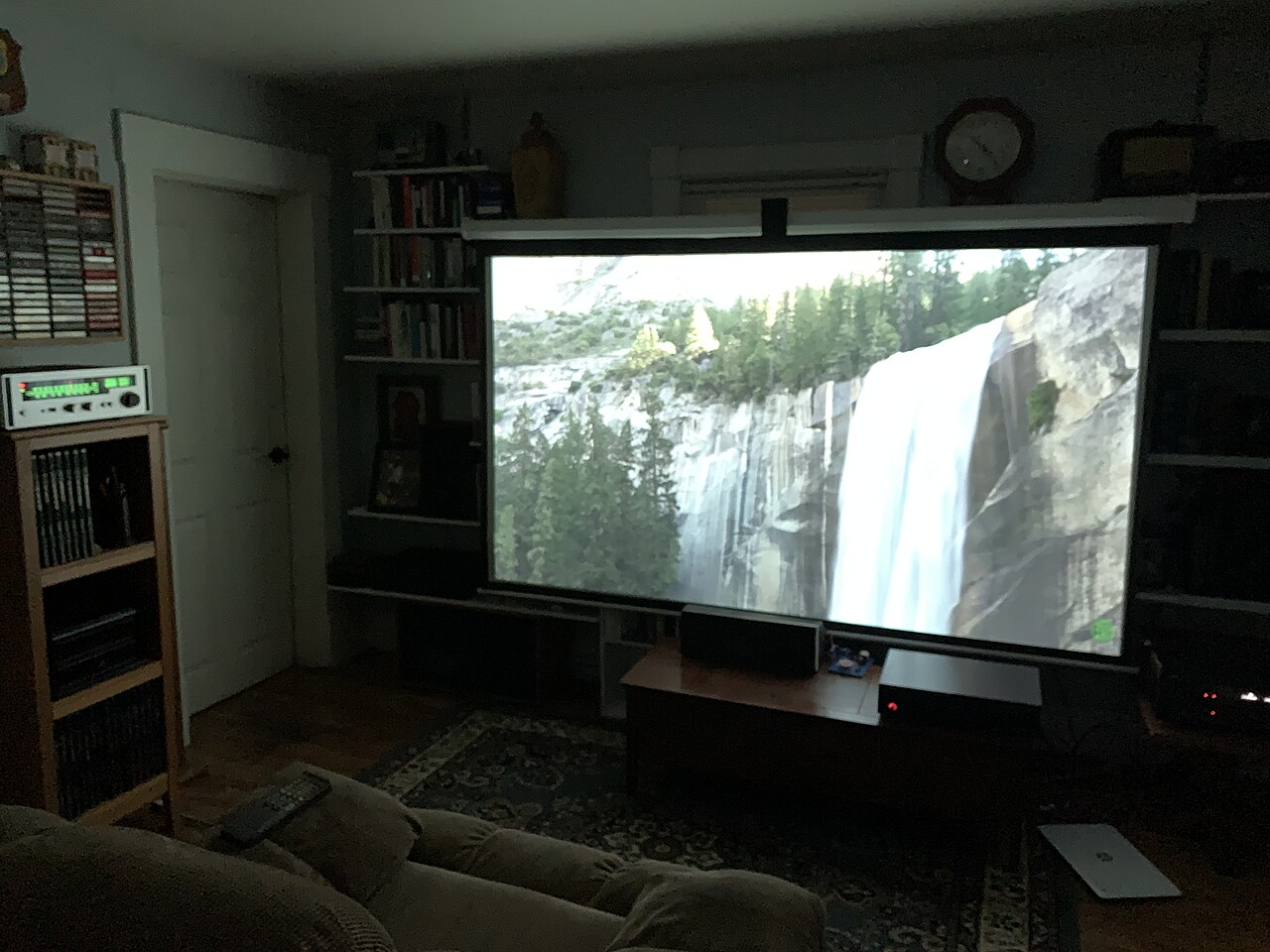 A pull-down projector screen in a living room, showing a landscape image